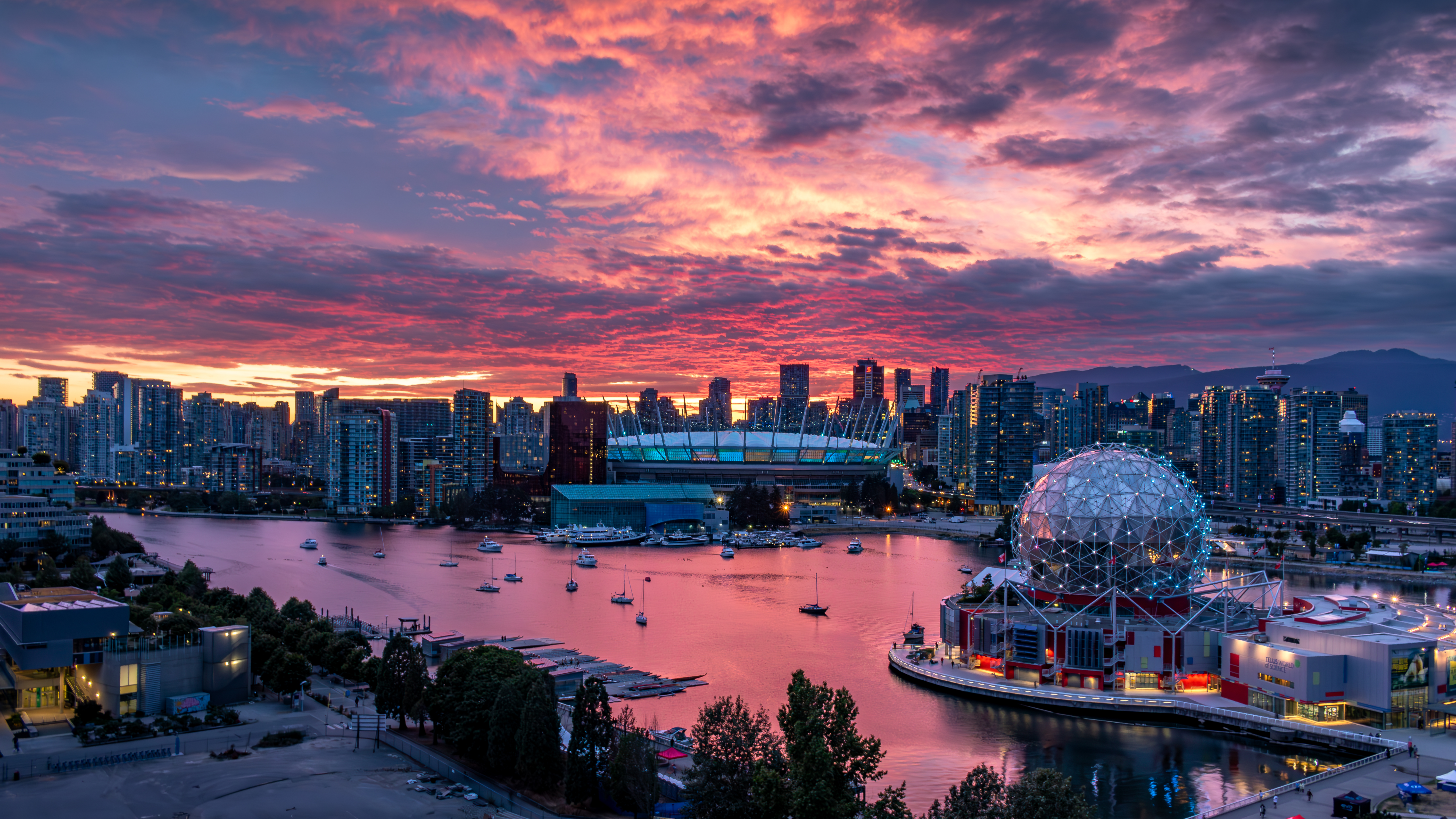 Vancouver's False Creek at sunset, with Science World, BC Place, the downtown skyline, and boats on the water under a brilliant pink and orange sky