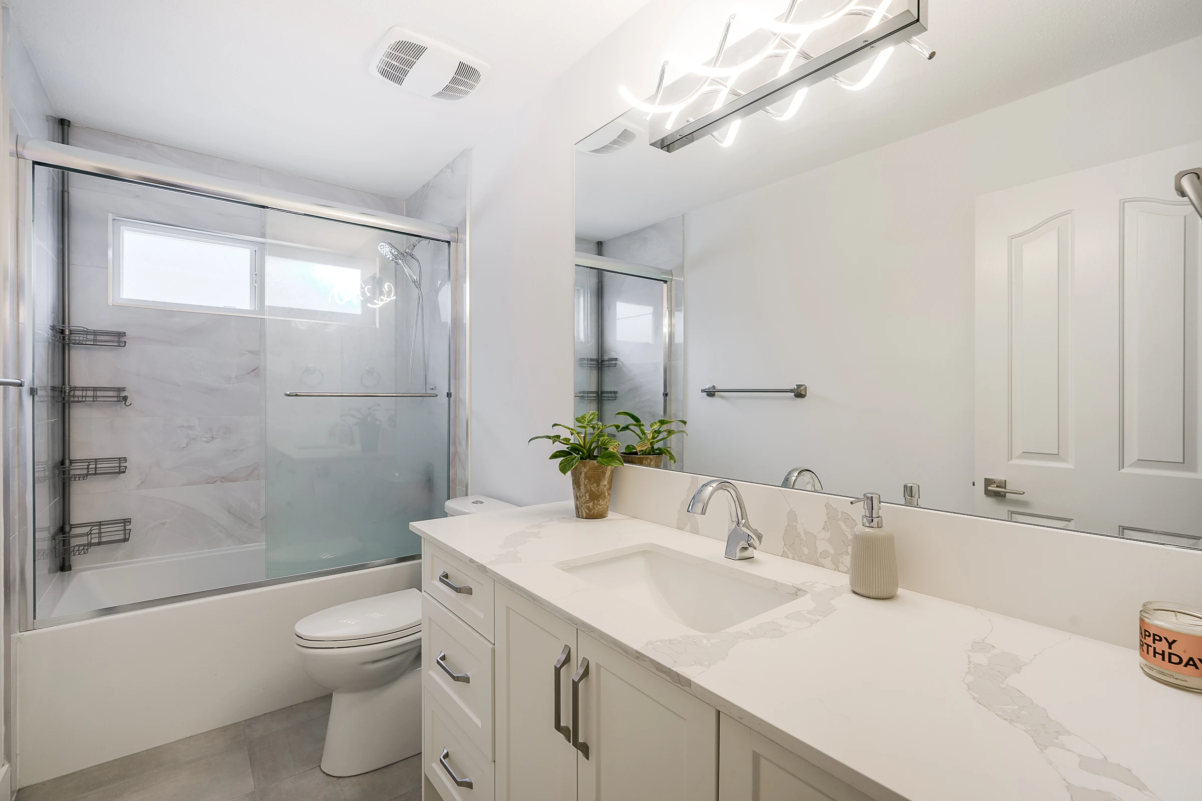 Bright white suite bathroom with quartz vanity, glass shower enclosure and modern lighting