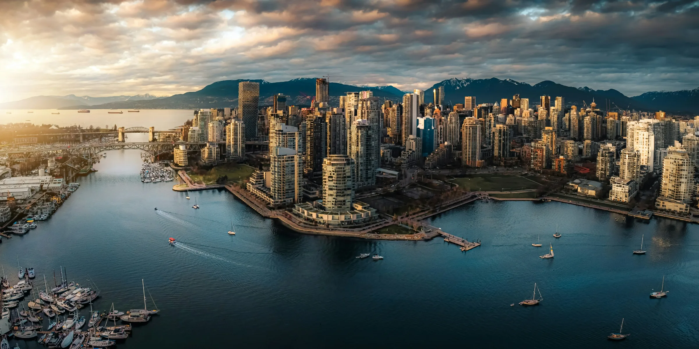 Aerial panorama of downtown Vancouver at sunset — False Creek marina and the city skyline against the snow-capped North Shore mountains