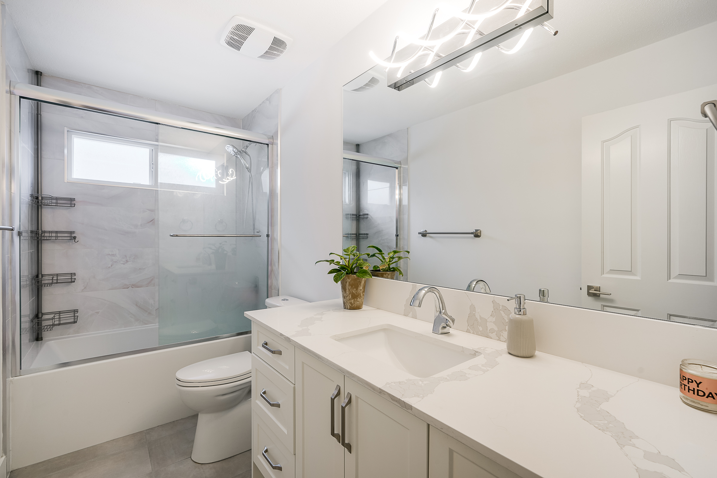 White bathroom with quartz vanity, glass shower and modern lighting