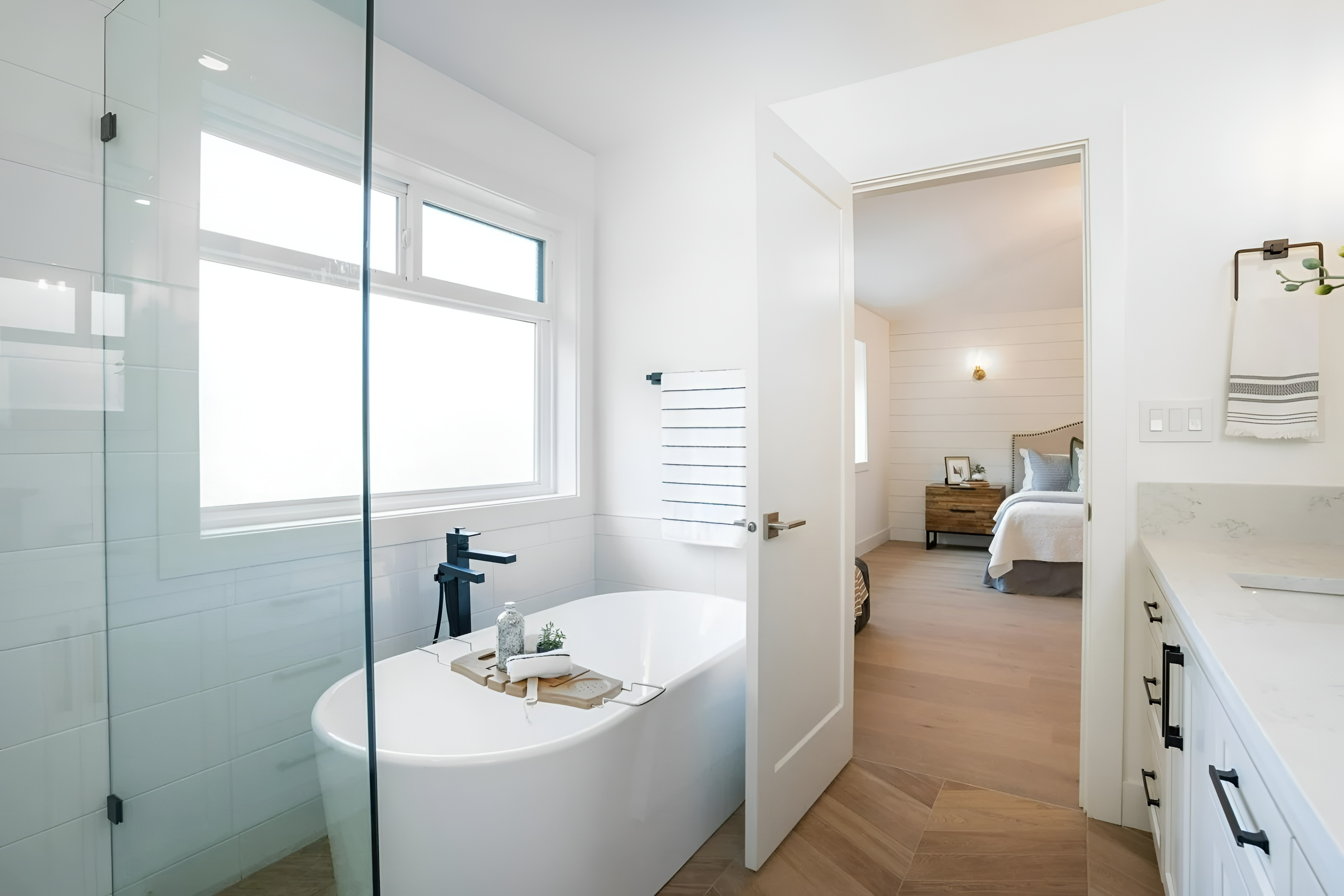 Bright white primary bathroom with freestanding soaker tub and view through to the bedroom