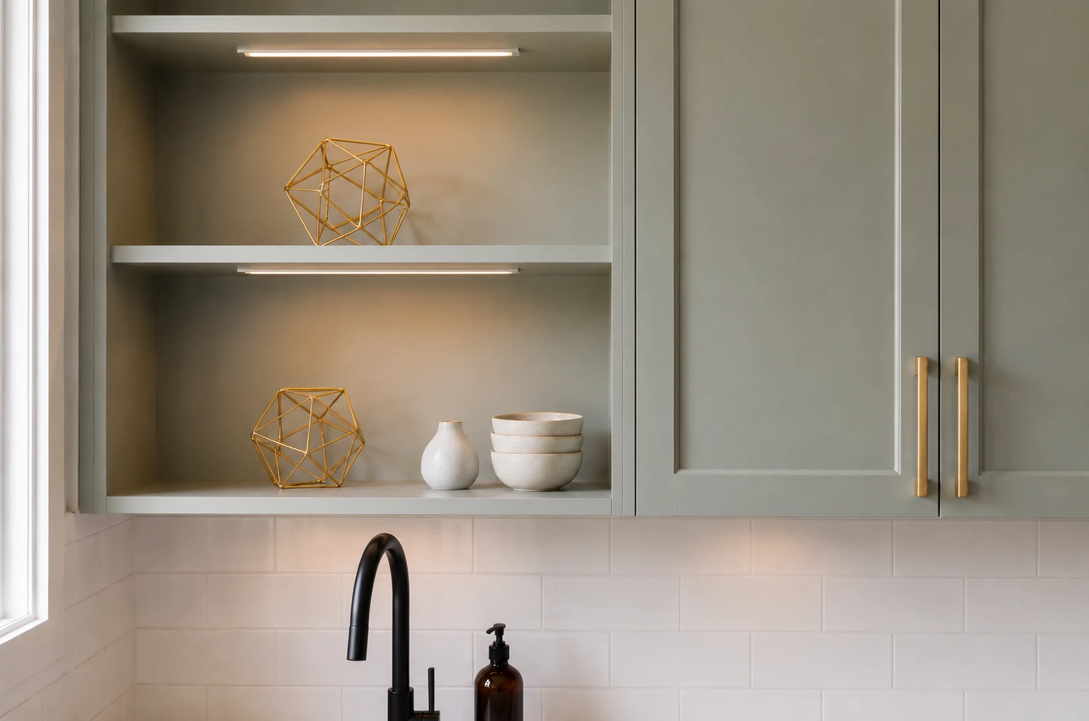 Sage-green shaker cabinets with brass pulls, open shelving and subway tile backsplash