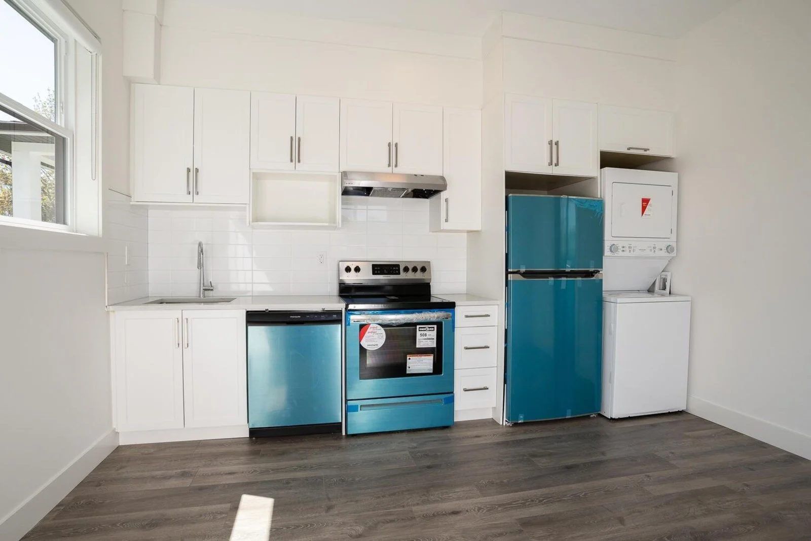 Legal suite kitchen with white shaker cabinetry, full-size range and stacked laundry